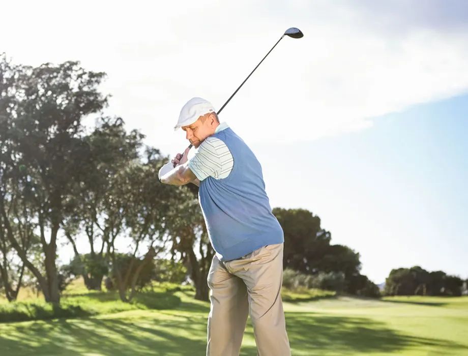 Man in golf attire tees off on the sunny Schloss Karnitz golf course while on vacation at the Grand Hotel Binz.