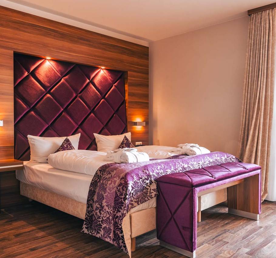 Doppelbett in der Ferienwohnung in Binz auf Rügen mit weinrotem Kopfteil und Tagesdecke.