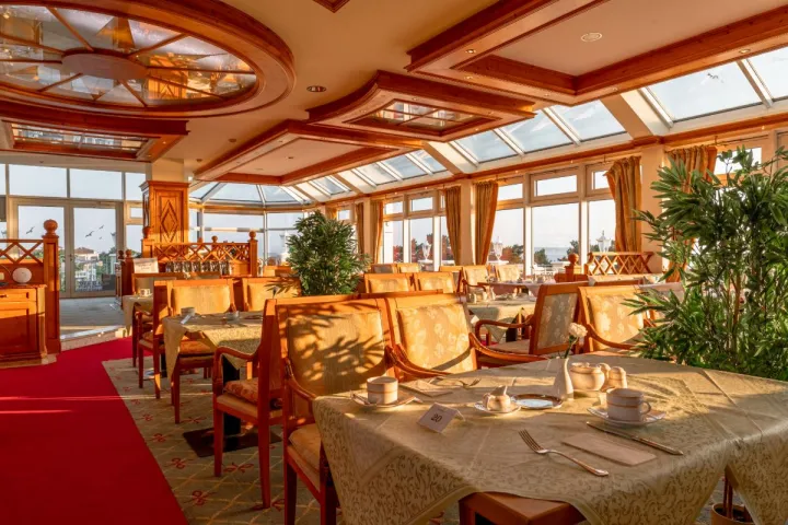 The spacious, elegantly furnished dining area with chairs, tables and panoramic windows in the Königsstuhl restaurant.