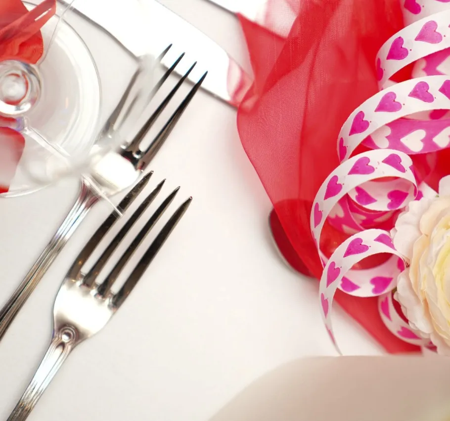 Detailaufnahme einer romantischen Valentinstag-Tischdekoration mit Herzbändern, rotem Stoff und festlichem Besteck im Arkona Strandhotel.