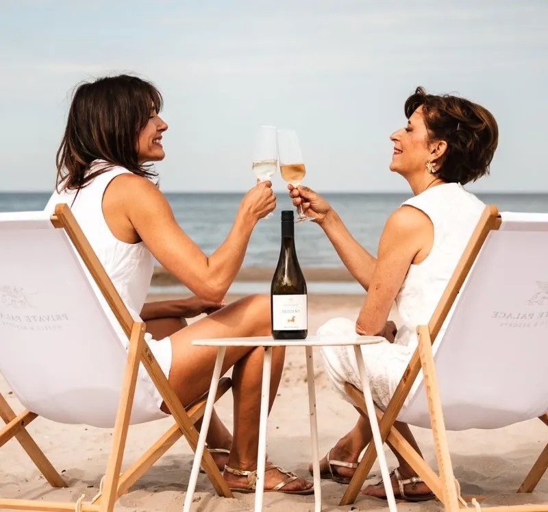 Two women toasting their holiday together with sparkling wine on a beach on Rügen