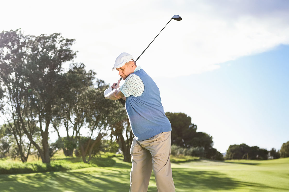 Mann in Golfkleidung schlägt auf dem sonnigen Golfplatz Schloss Karnitz während des Urlaubs im Grand Hotel Binz ab.